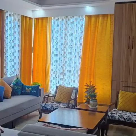 Living room with mustard curtains layered over printed sheers, a sculptural loop ceiling pendant