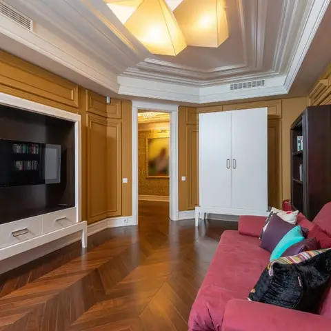 Living room with mustard-gold moulded wall panelling, herringbone wood flooring, a coffered ceiling with a faceted pendant light, and a magenta velvet sofa