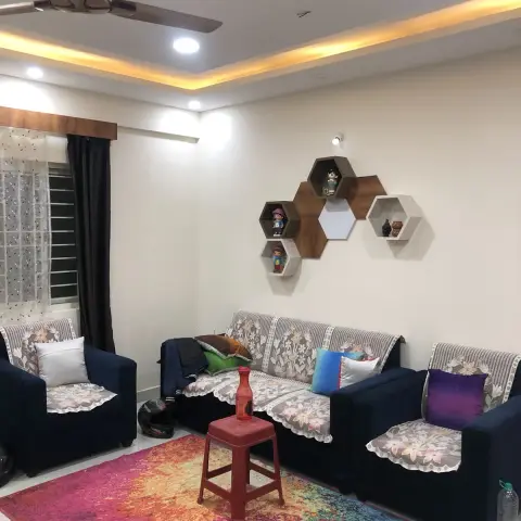 Living room with navy sofas dressed in floral lace covers, a colourful gradient rug, and a hexagonal honeycomb display shelf styled with figurines