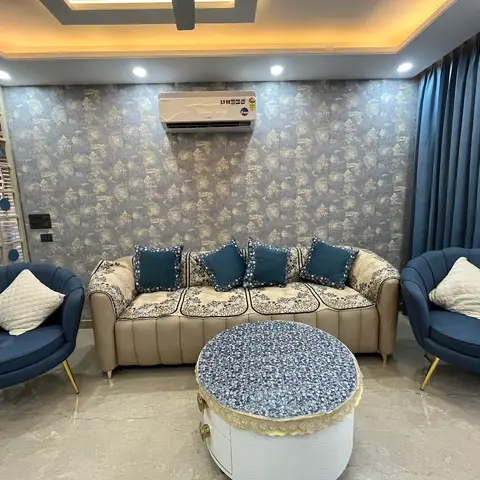 Living room with navy velvet shell armchairs on brass legs, a beige sofa styled with a floral throw cover, and a round tufted coffee table