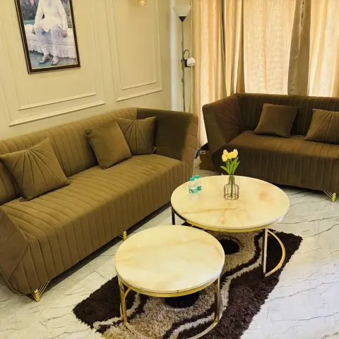 Living room with olive green channel-tufted velvet sofas, gold-framed marble nesting coffee tables and panel-moulded walls.