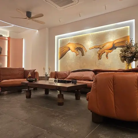 Living room with plush terracotta leather channel-tufted sofas on wood block legs, a large backlit Creation-of-Adam mural