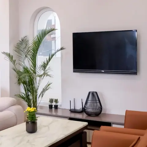 Living room with rust leather armchairs, a marble-top coffee table and a wall-mounted TV above a low console beneath an arched window