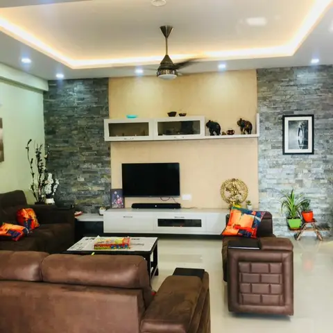 Living room with stacked stone cladding flanking a cream TV wall, a glass display shelf above, and brown leather sofas around a coffee table.
