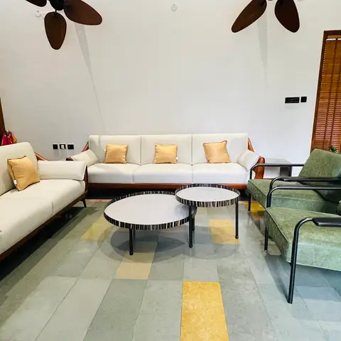 Living room with tan leather and cream sofas, olive-green mid-century armchairs, and twin round marble coffee tables on a stone floor with ochre-yellow inlay