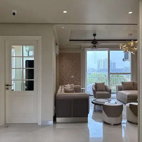 Living room with taupe ribbed-velvet sofas and swivel armchairs beneath a gold leaf sculptural chandelier, floor-to-ceiling city view behind.