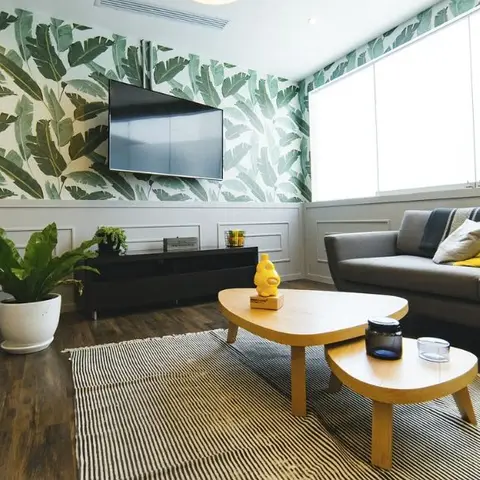 Living room with tropical leaf-print wallpaper above wainscot panelling, a grey sofa with yellow accent cushions