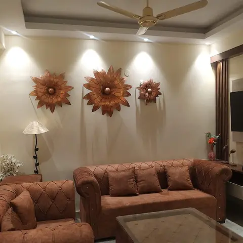 Living room with tufted brown chesterfield-style sofas facing a TV console, three copper sunflower wall sculptures lit by spotlights above