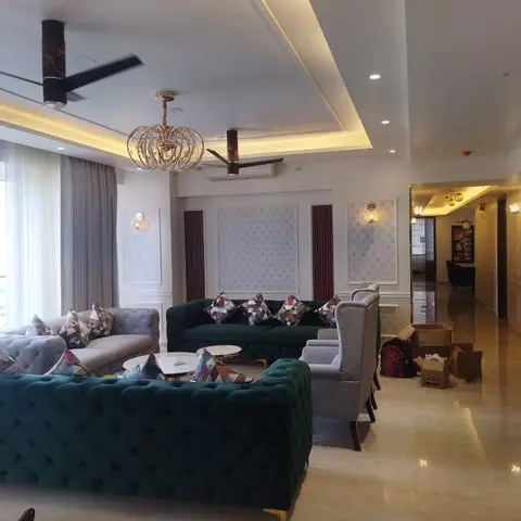 Living room with tufted emerald-green velvet sofas and a gold ring-tier chandelier, moving boxes still on the floor