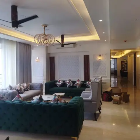 Living room with tufted emerald-green and grey Chesterfield-style sofas beneath a tiered cove-lit POP ceiling and a birdcage chandelier.