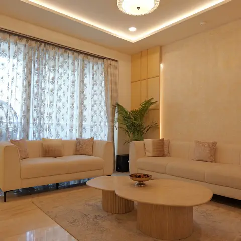 Living room with two cream channel-tufted sofas facing a pair of round travertine pedestal coffee tables, patterned sheer curtains