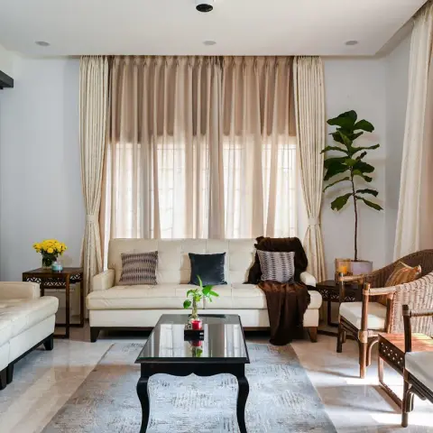 Living room with two cream tufted leather sofas facing a black lacquered coffee table on a pale grey rug, cane-and-teak armchairs by the window