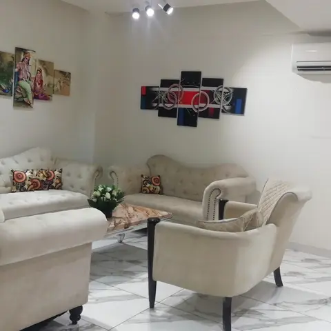 Living room with two cream tufted chesterfield sofas and a matching armchair around a marble-top coffee table, beneath a gallery wall of framed art panels.