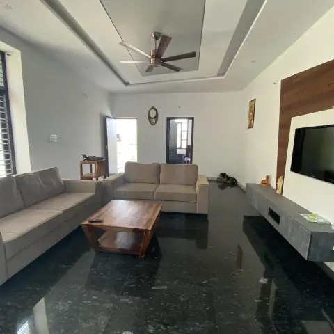 Living room with two grey fabric sofas around a sheesham-wood coffee table, facing a wall-mounted TV on a walnut-panel feature wall with a floating