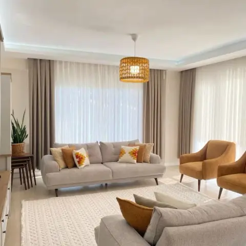 Living room with two grey upholstered sofas dressed in mustard and cream cushions, a pair of mustard velvet armchairs, a rattan drum pendant light