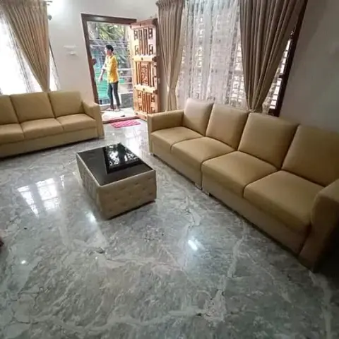 Living room with two mustard leather sofas around a tufted coffee table on polished grey marble flooring, carved wooden main door visible beyond