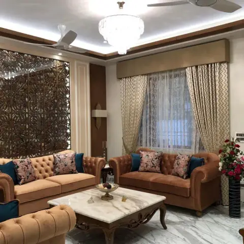 Living room with two tan velvet chesterfield sofas and floral-and-teal cushions around a carved-leg white marble coffee table