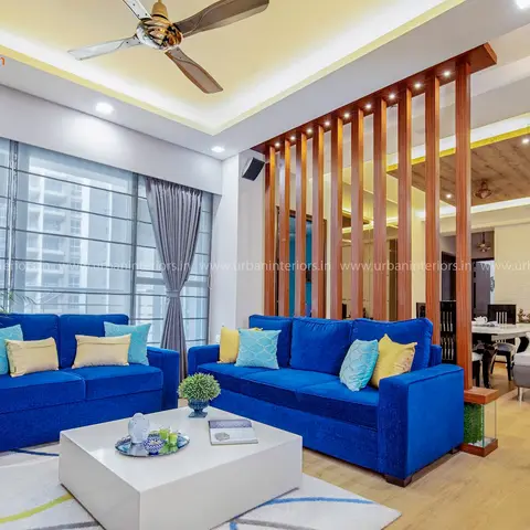 Living room with vivid blue sofas facing a floating white coffee table, separated from the dining area by a vertical teak wood slat partition under a layered