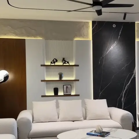Living room with white boucle sofas around a round marble pedestal coffee table, a backlit fluted niche with floating display shelves