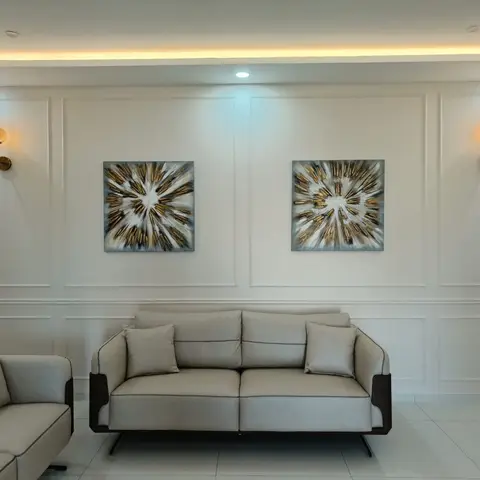 Living room with white wainscot wall panelling, twin brass wall sconces, and matching gold starburst artworks flanking a beige sofa.