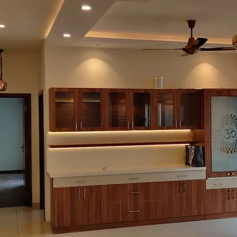 Living space with a wall-length wood-veneer crockery unit featuring a glass door etched with an Om motif and LED shelf lighting