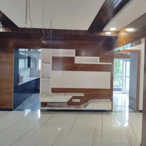 Living space with a wood-clad ceiling beam and a wood-and-white-tile TV feature wall, opening into a dark blue kitchen through a glass partition