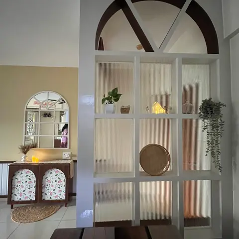 Living space with an arched fluted-glass grid room divider styled with plants and curios, beside a floral-front console table under an arched paned mirror.