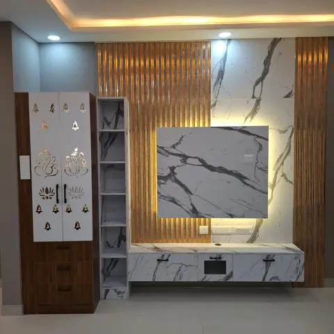 Living wall combining a wood-and-white pooja cabinet with brass Ganesh motifs beside a large marble-clad TV panel framed in gold fluted trim