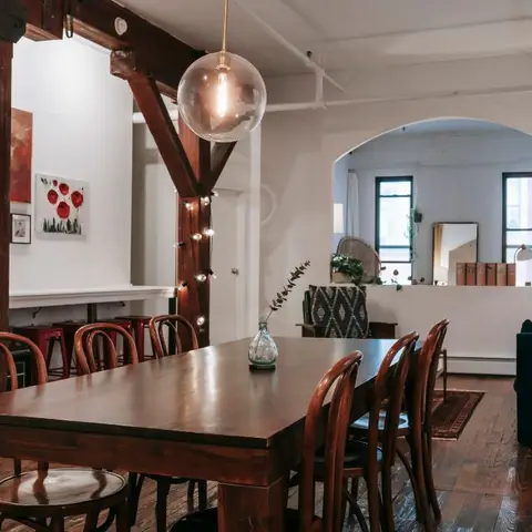 Loft-style dining area under exposed timber beams with a glass globe pendant and a gallery wall of framed art.