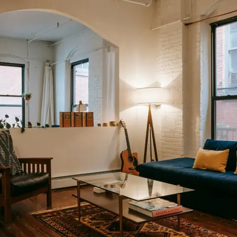 Loft-style living room with a whitewashed exposed-brick archway, navy velvet sofa with mustard cushions, a glass-and-brass coffee table