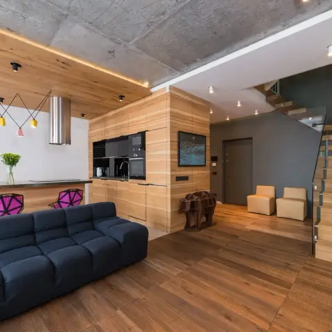 Loft-style open plan under a raw board-marked concrete soffit, where an ash-veneer volume wraps the kitchen run and folds onto the ceiling