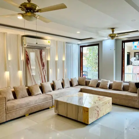 Long beige velvet L-sofa with gold-trimmed bases facing a red-veined onyx-look block coffee table