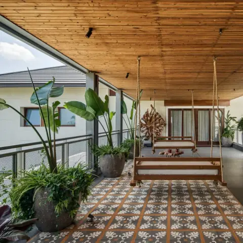 Long covered verandah with a teak rope swing hung over a runner of terracotta-and-grey patterned cement tiles
