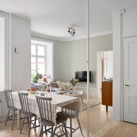 Long dining table with grey spindle-back chairs and a linen runner beside tall period windows