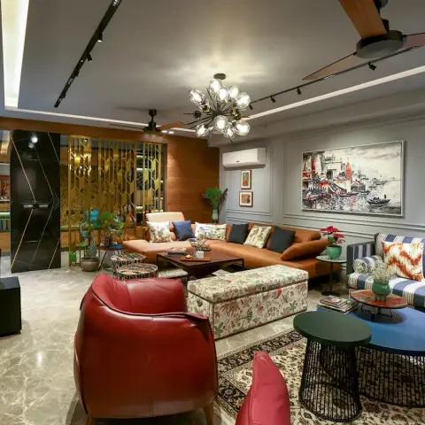 Long eclectic living room where a brass geometric jaali screen separates a lit book niche from a tan leather sectional, facing a striped blue settee