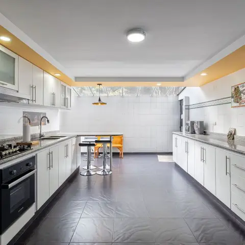 Long galley kitchen with white cabinetry, granite counters, a yellow accent ceiling band, dark tile flooring