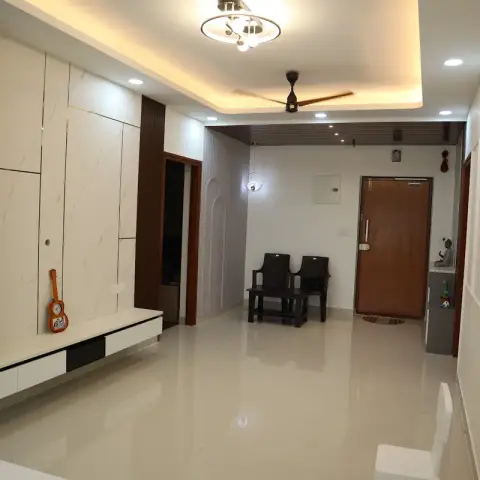 Long living hall with a marble-slab TV wall and grey display niches on the left running down to the teak main door