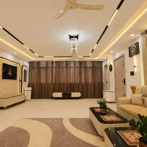 Long living room lit by recessed ceiling profile strips and a rectangular linear pendant: cream quilted leather sofa, black-topped nesting tables