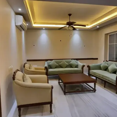 Long living room with a carved teak sofa set upholstered in sage green and cream around a glass-topped wooden coffee table