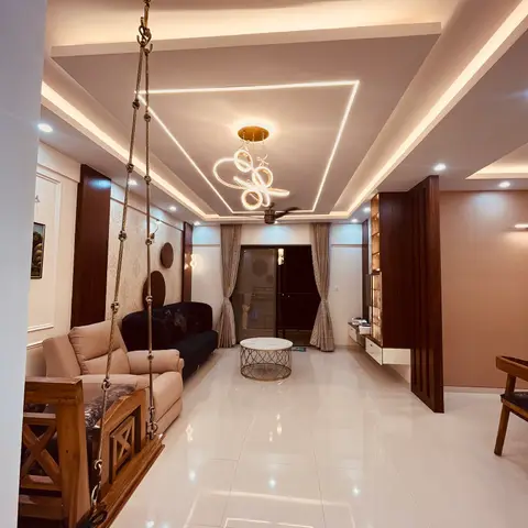 Long living room with a traditional wooden hanging swing beside black and beige sofas, a multi-tier cove-lit POP ceiling with a sculptural pendant