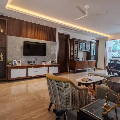 Long living room with the TV on a grey marble slab framed by dark fluted wood panelling, a lit glass-shelf niche of brass idols to its left