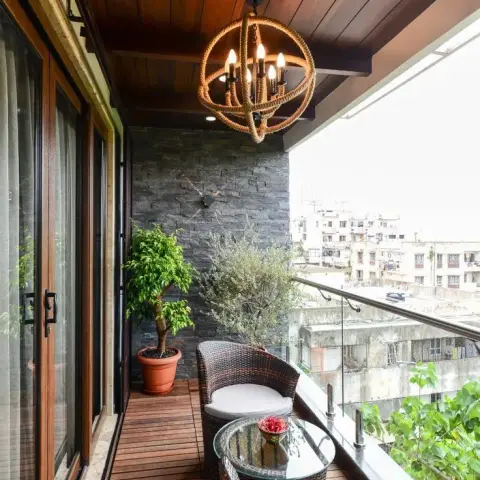Long narrow apartment balcony decked and ceiled in stained teak, with a rope-wrapped orb chandelier over two rattan tub chairs and a glass side table