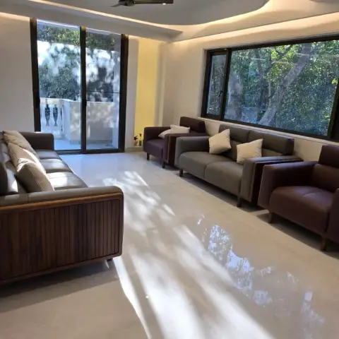 Long, still-unstyled living room where a curved cove-lit POP border frames the ceiling and afternoon tree shadows fall across cream polished marble between two