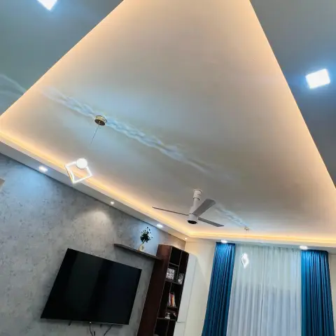 Looking up in a living room at a large triangular POP ceiling drop outlined in warm cove light