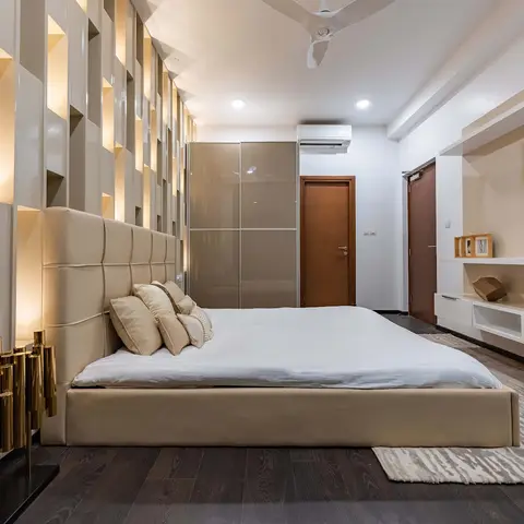 Low beige bed with a tall square-tufted leather headboard, backed by a grid of backlit vertical niches