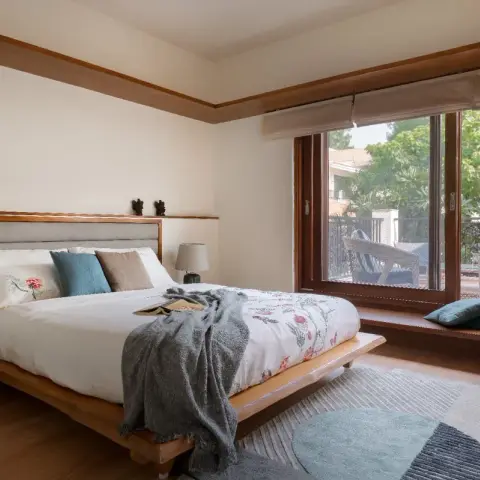 Low teak platform bed with a grey channel-tufted headboard set into a wall-mounted wooden ledge, a grey knit throw pulled across a floral duvet