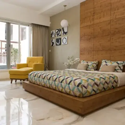 Low wooden platform bed against a full-height veneer headboard wall, with a mustard armchair