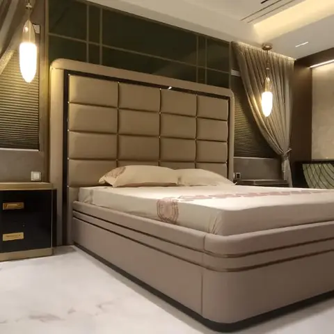 Luxury bedroom with a tall champagne tufted-leather bed and matching upholstered base, a black-and-gold nightstand