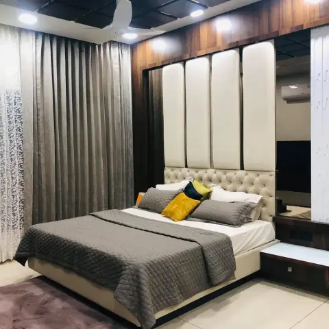 Luxury bedroom with a tall cream tufted-and-panel headboard against a wood-clad wall, wood-panelled ceiling with recessed lighting