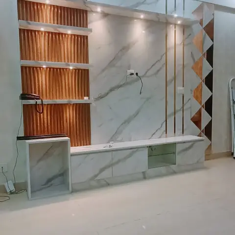 Marble-clad TV wall with backlit copper-toned fluted display shelving and a brass diamond-inlay accent strip, still mid-installation with exposed wiring.